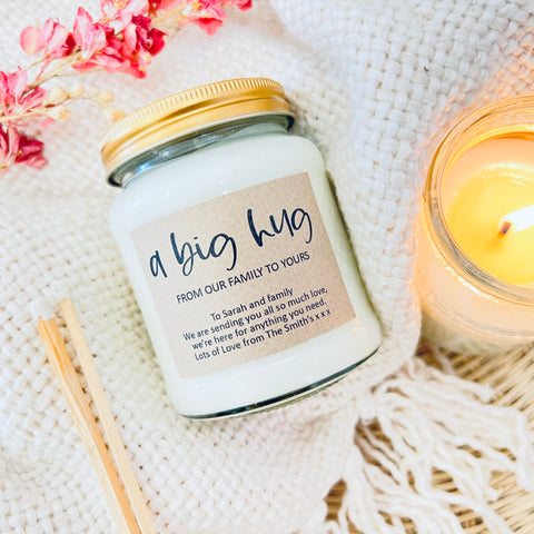 A Big Hug From Our Family To Yours - Scented Soy Wax Candle - Personalised. A glass jar candle on a wool blanket with flowers in the background.