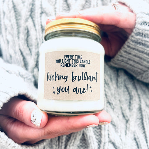 Hands holding scented soy wax candle in clear glass jar.