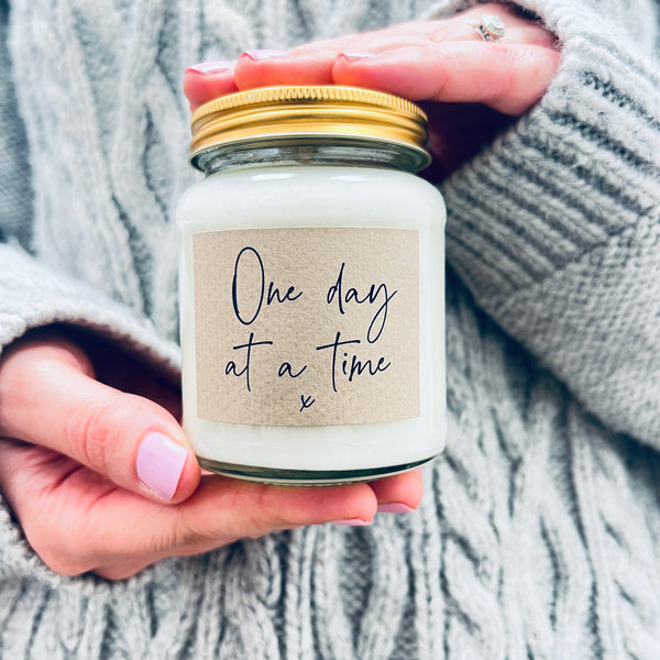Hands holding a scented soy wax candle in a jar.