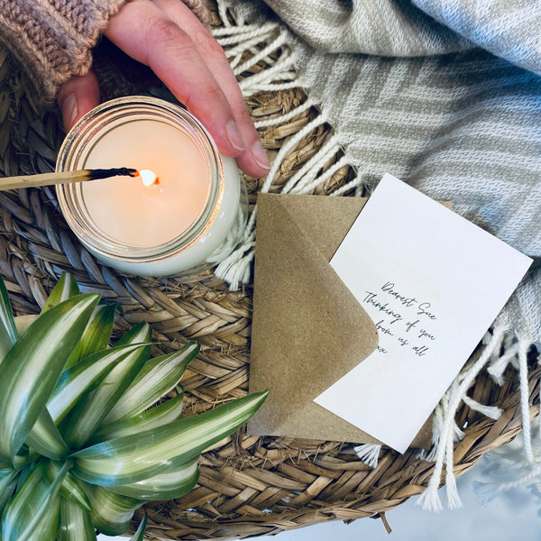 A gift card next to a lit glass jar soy wax candle. 