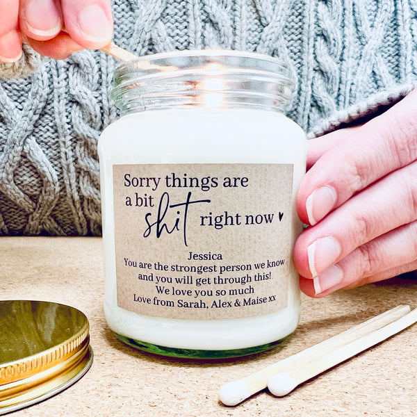 Someone lighting a glass jar candle that is sitting on a wool blanket with some flowers. 